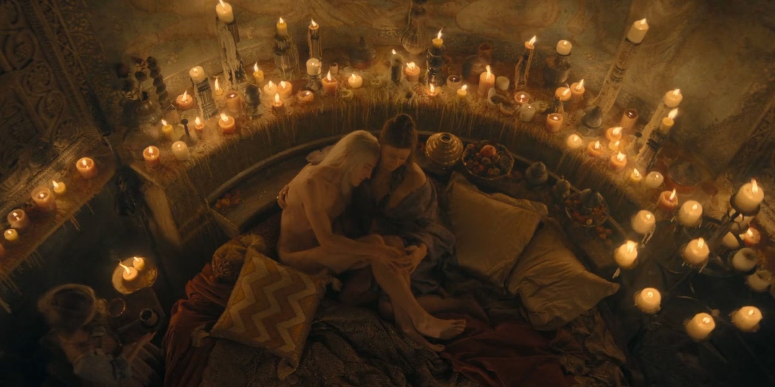 Aemond naked and swaddled by Sylvi on a bed surrounded by candles, in Season 2 Episode 2 of House of the Dragon