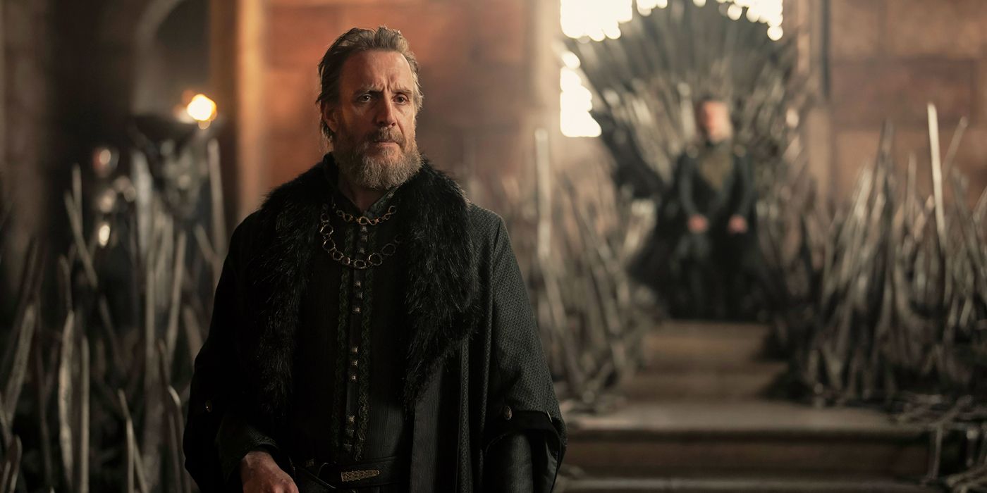 Rhys Ifans as Otto Hightower standing center frame, with Aegon sitting on the Iron Throne in the background, in House of the Dragon Season 2