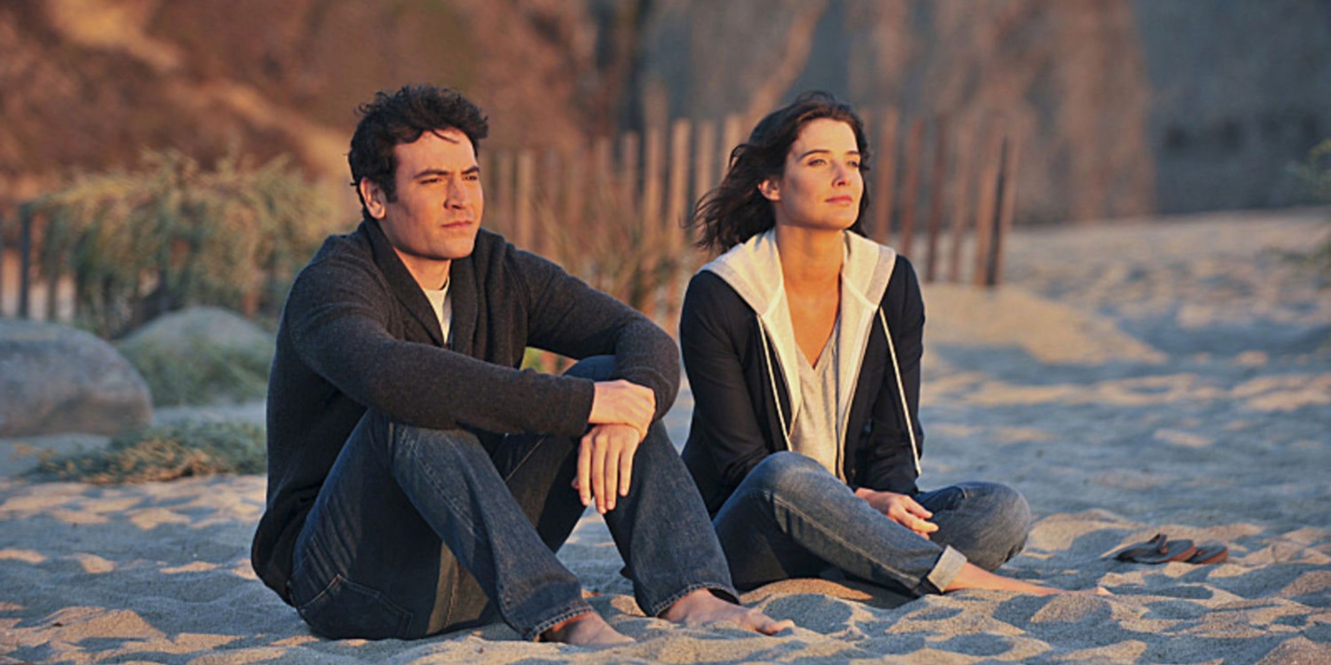 Ted and Robin sit next to one another on a beach looking at the ocean in How I Met Your Mother