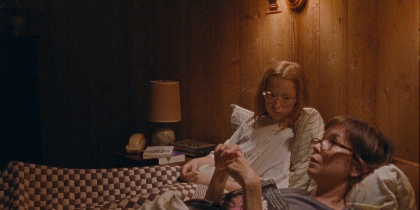Zoe Ziegler as Lacy and Julianne Nicholson as Janet laying in a bed talking in a still from Janet Planet. 