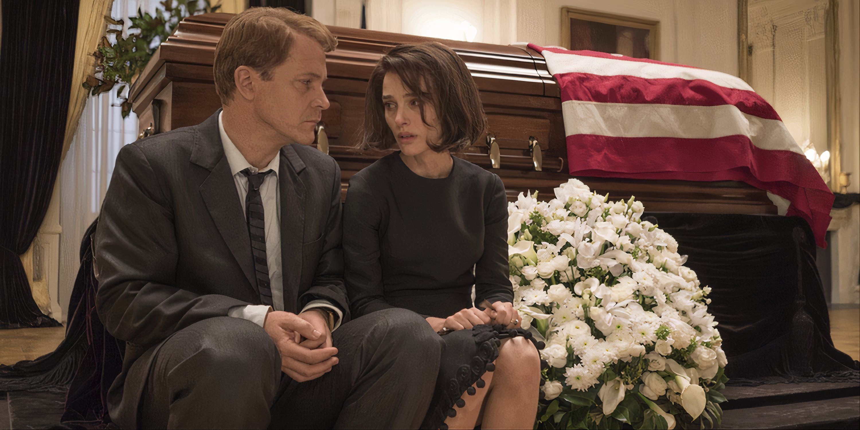 Peter Sarsgaard sitting next to Natalie Portman in front of a coffin in Jackie
