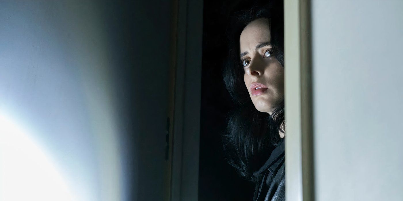 Jessica Jones (Krysten Ritter) staring around a dark corner on the right as her flashlight illuminates part of the wall on the left