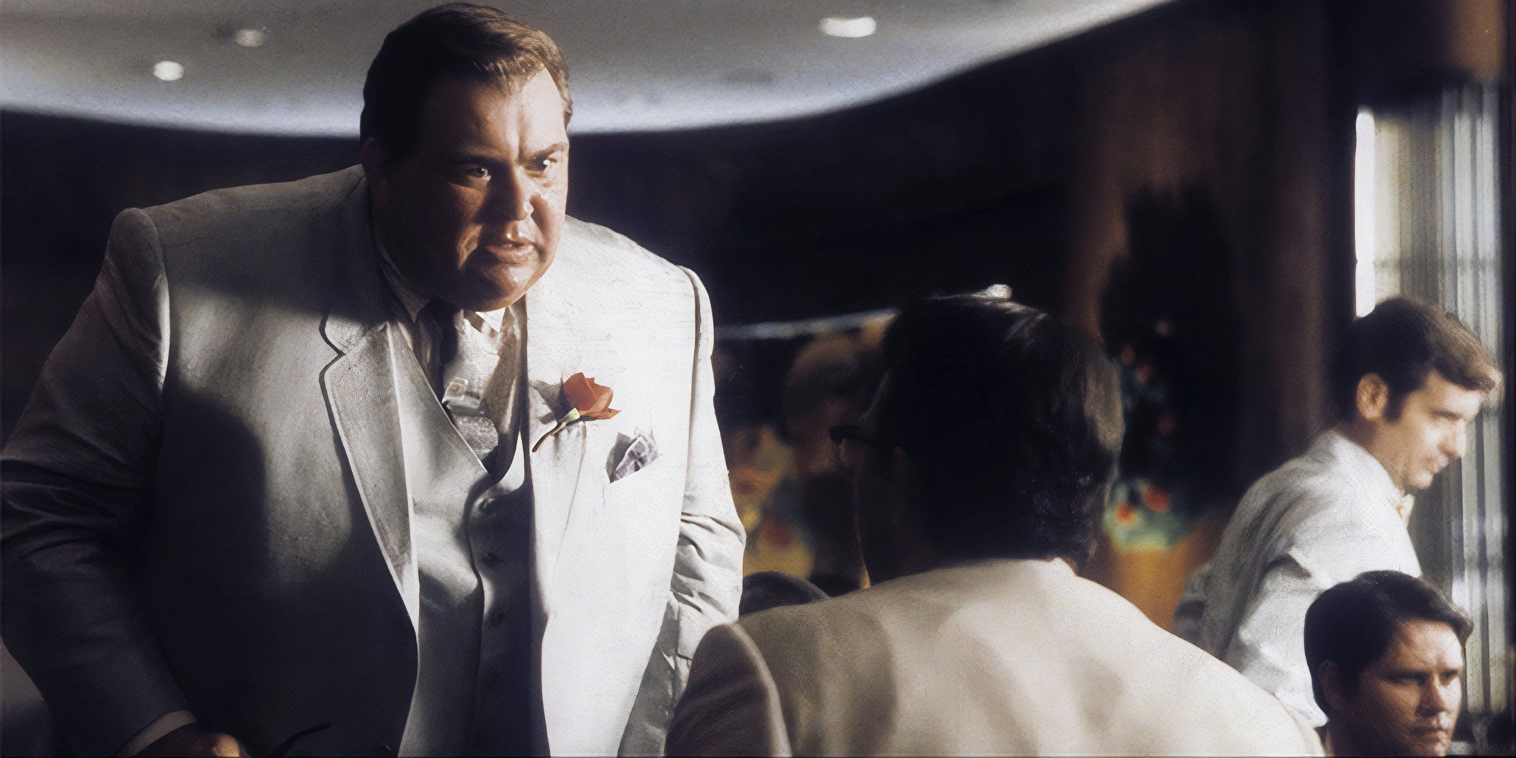 John Candy in a white suit talking to someone in a restaurant in JFK