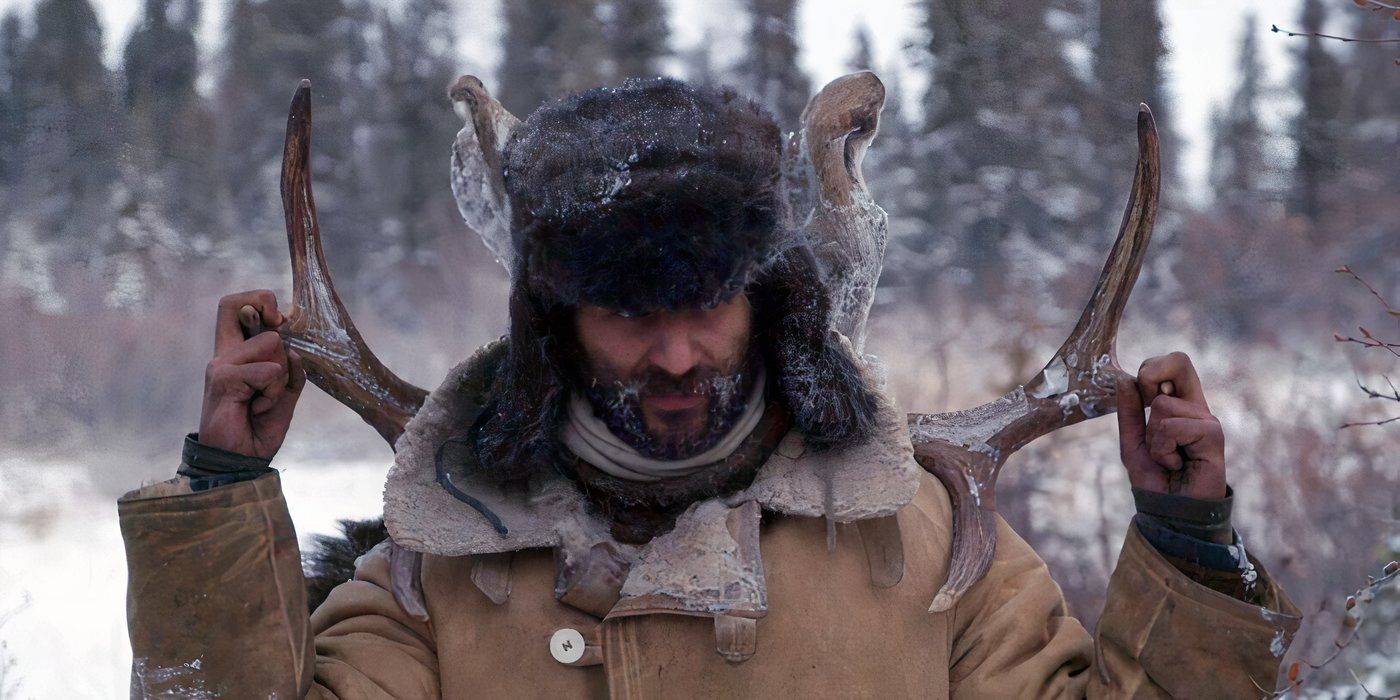 A man wearing a fur hat and heavy winter coat carries antlers on his back across a snowy landscape