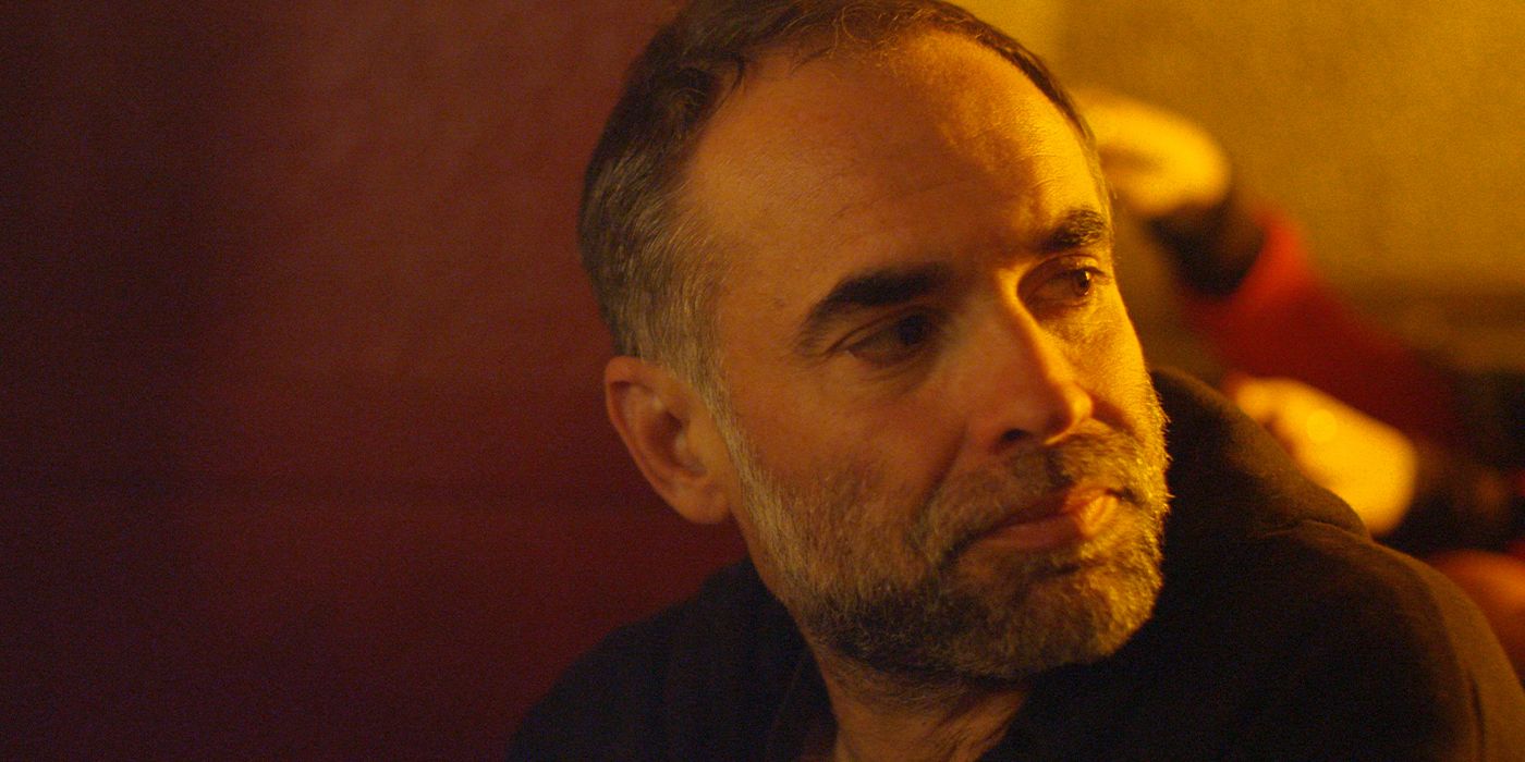 Headshot of director Karim Aïnouz looking to his right in orange lighting