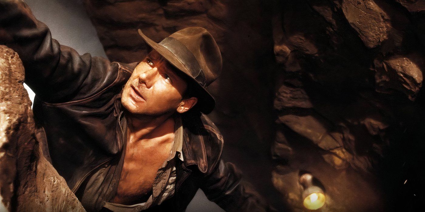 Indy (Harrison Ford) hangs off of a cliff by one hand. On a ledge below him is the Holy Grail