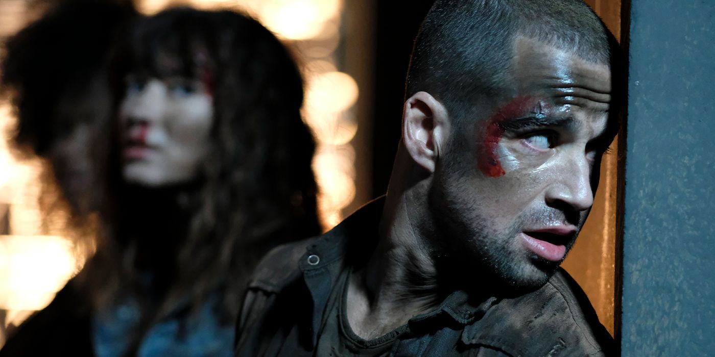 A bloody Rupert Lazarus as Alex, peeking around a corner with his friends blurred in the background in Lumina