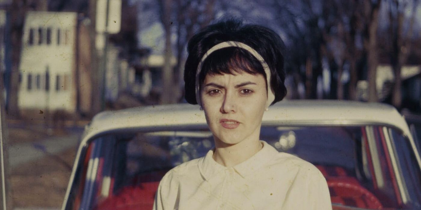 A woman looks at the camera with a curious expression in front of a car