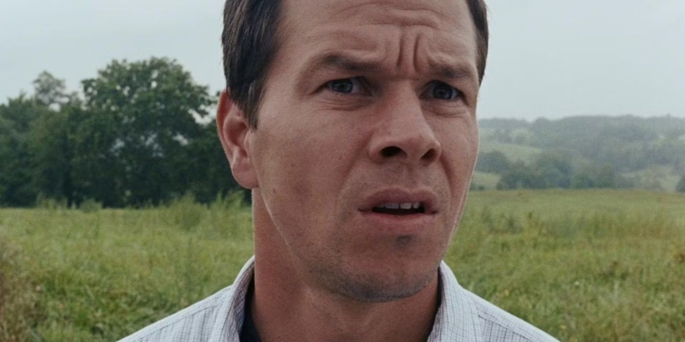 Mark Wahlberg, standing on a grassy field, frowning into the distance in The Happening