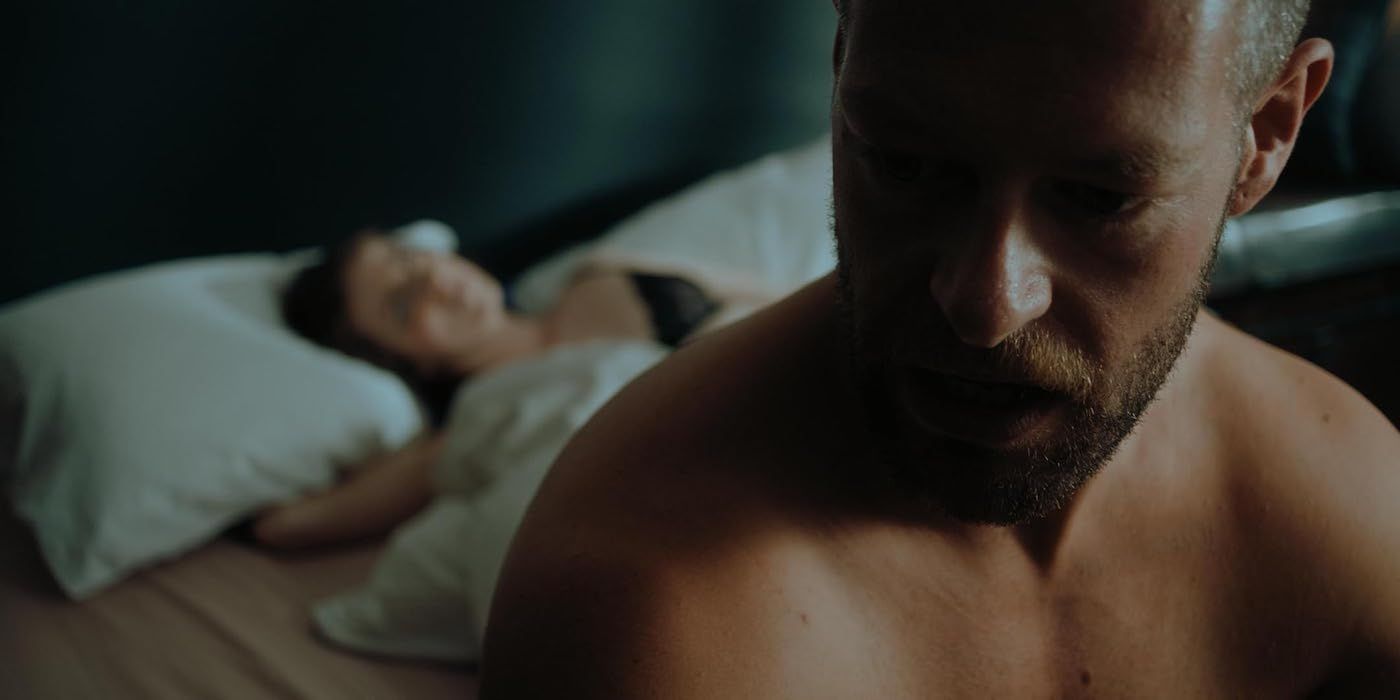 En Kill Your Lover, un hombre se sienta en una cama y una mujer yace detrás de él. 