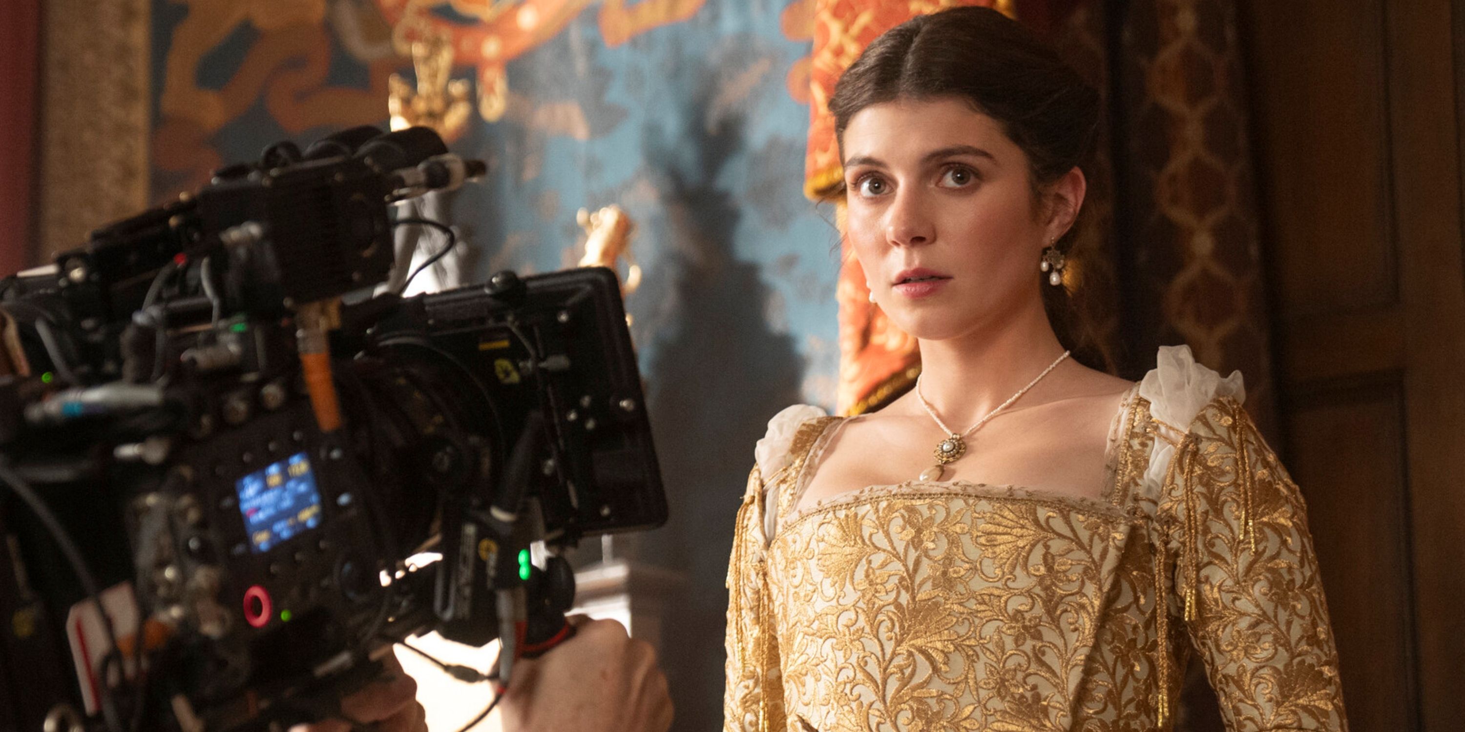 Emily Bader as Jane Grey in a gold dress in front of the camera that's shooting the scene for My Lady Jane