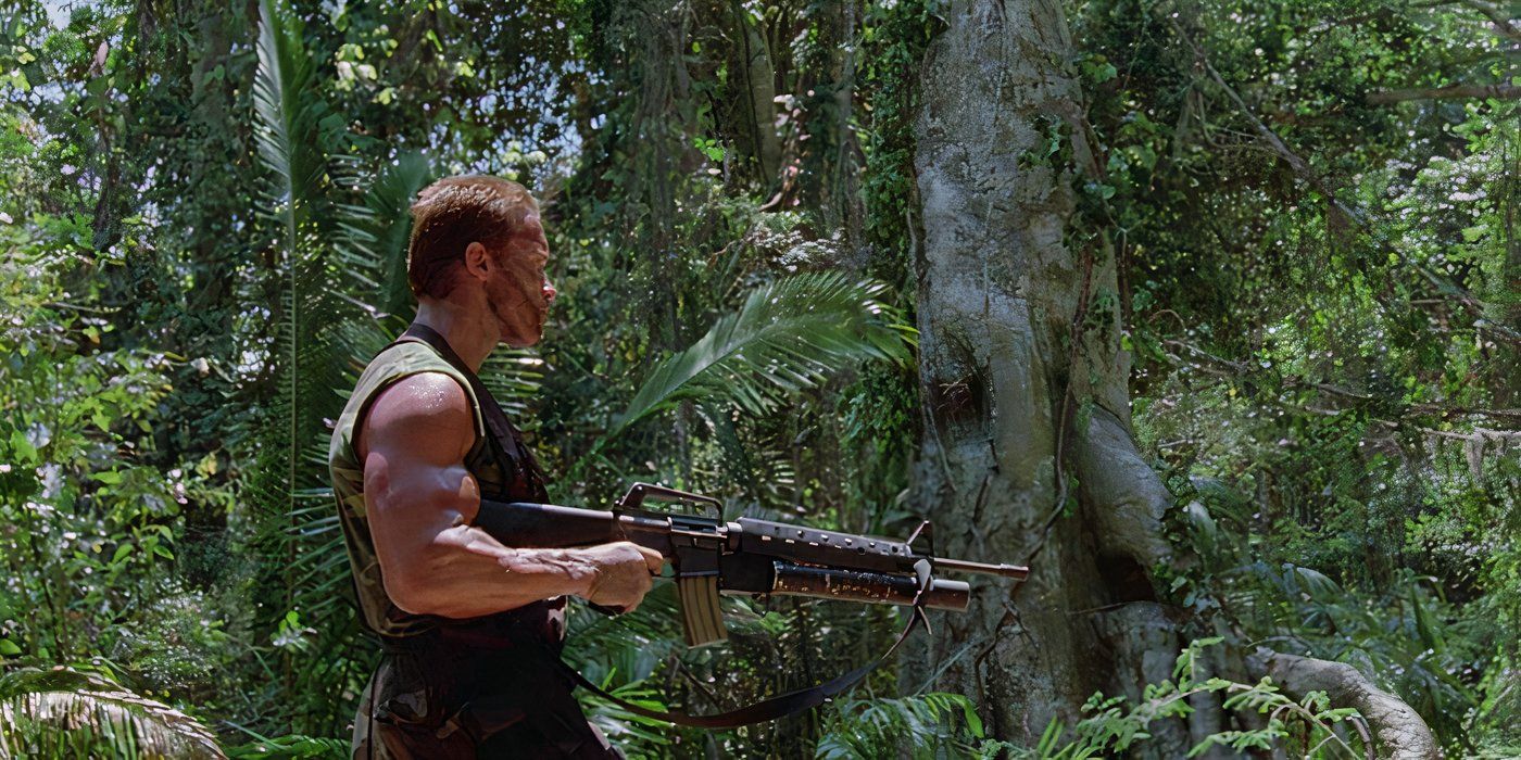 Dutch (Arnold Schwarzenegger) walks through the jungle holding a rifle