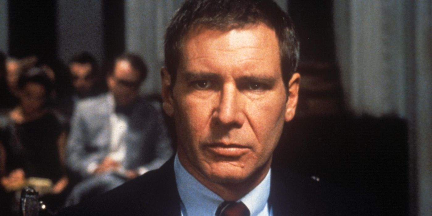 Harrison Ford as Rusty Sabich looking stern, sitting with people behind him in Presumed Innocent
