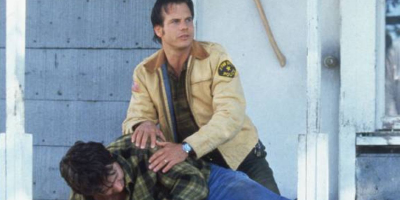 Bill Paxton as Dale wearing a police officer jacket holding a man down in 'One False Move'