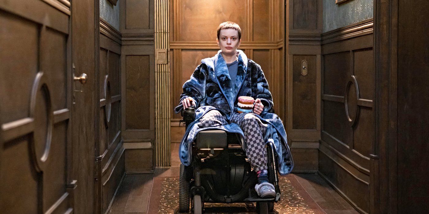 Ruth Codd as Anya, wearing a blue robe, sitting in a wheelchair, and holding a donut-shaped mug in The Midnight Club