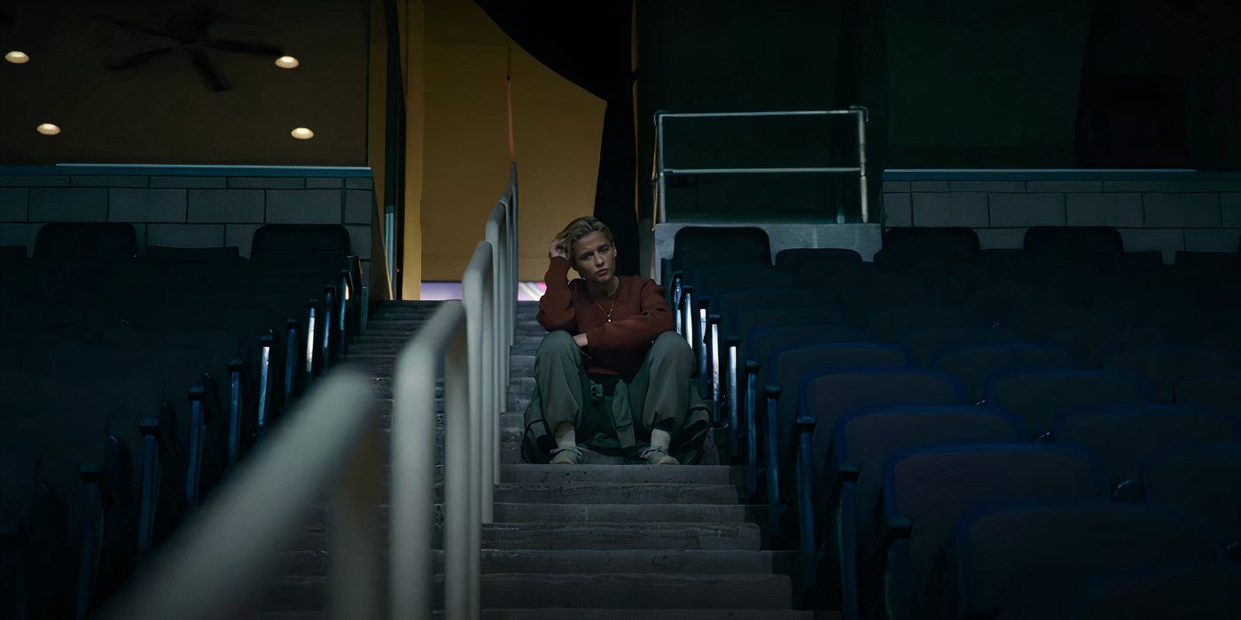 Naomi Scott se sienta sola en las escaleras de las gradas del estadio en la película 