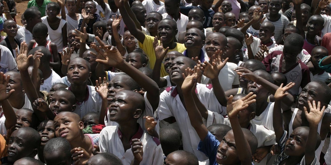 A tightly-packed crowd of Rwandan civilians raises their hands 