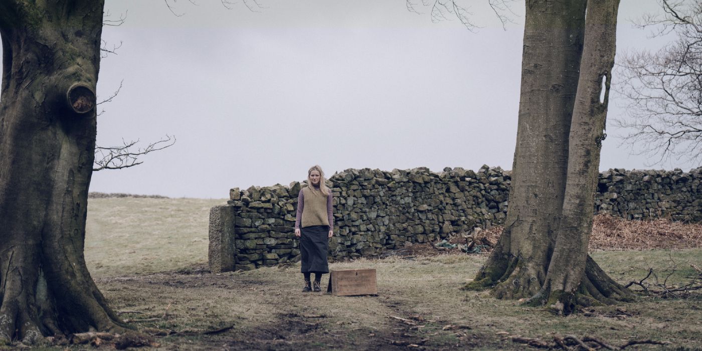 Morfydd Clark standing in the distance in front of a stone wall in Starve Acre