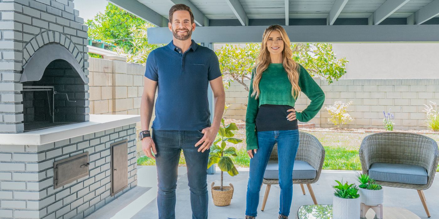 Tarek El Moussa and Christina Hall posing by an outside pizza oven in a patio