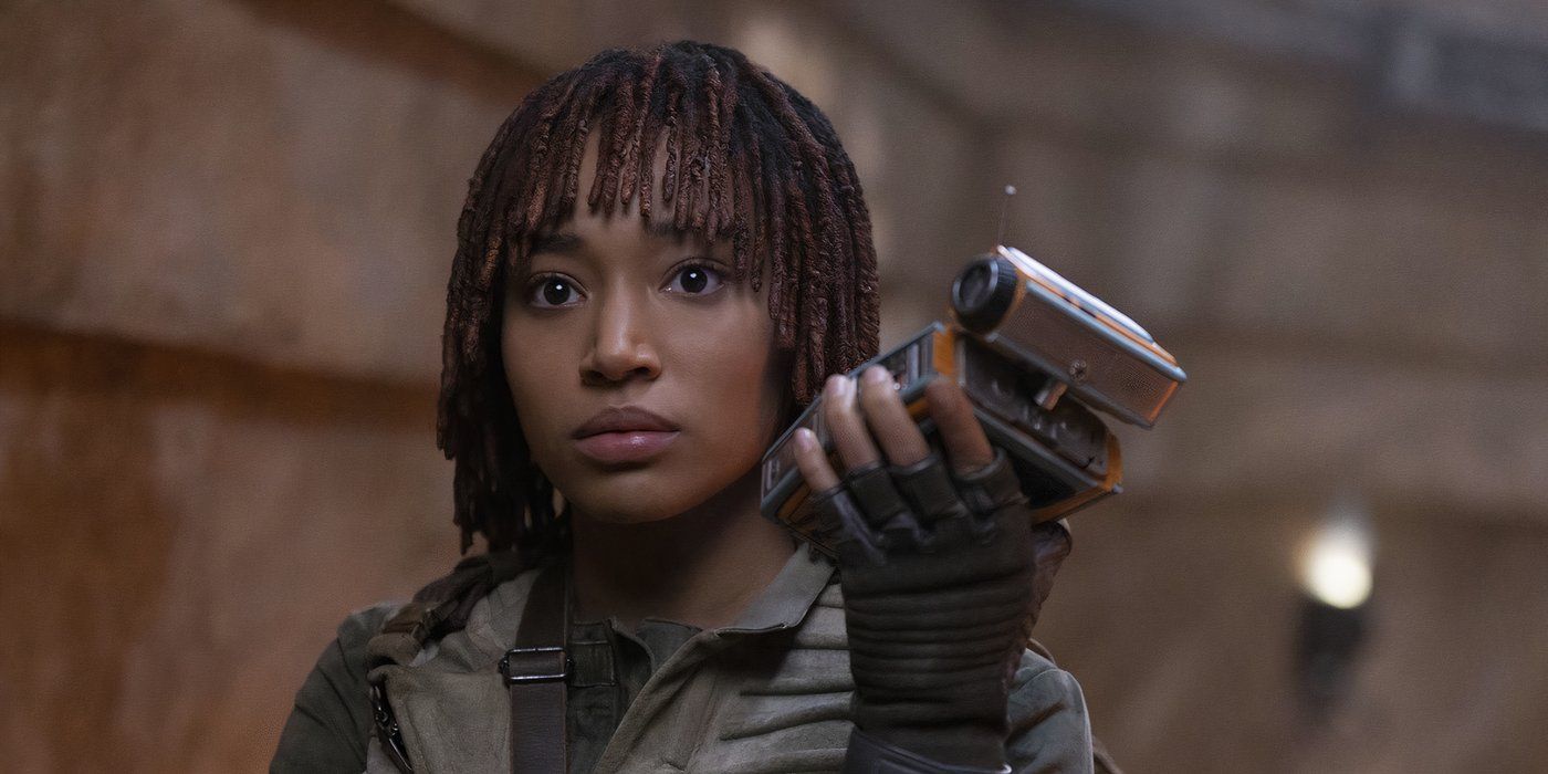 En The Acolyte, Osha (Amandla Stenberg) sostiene el droide Pip cerca de su cara y mira solemnemente hacia adelante.