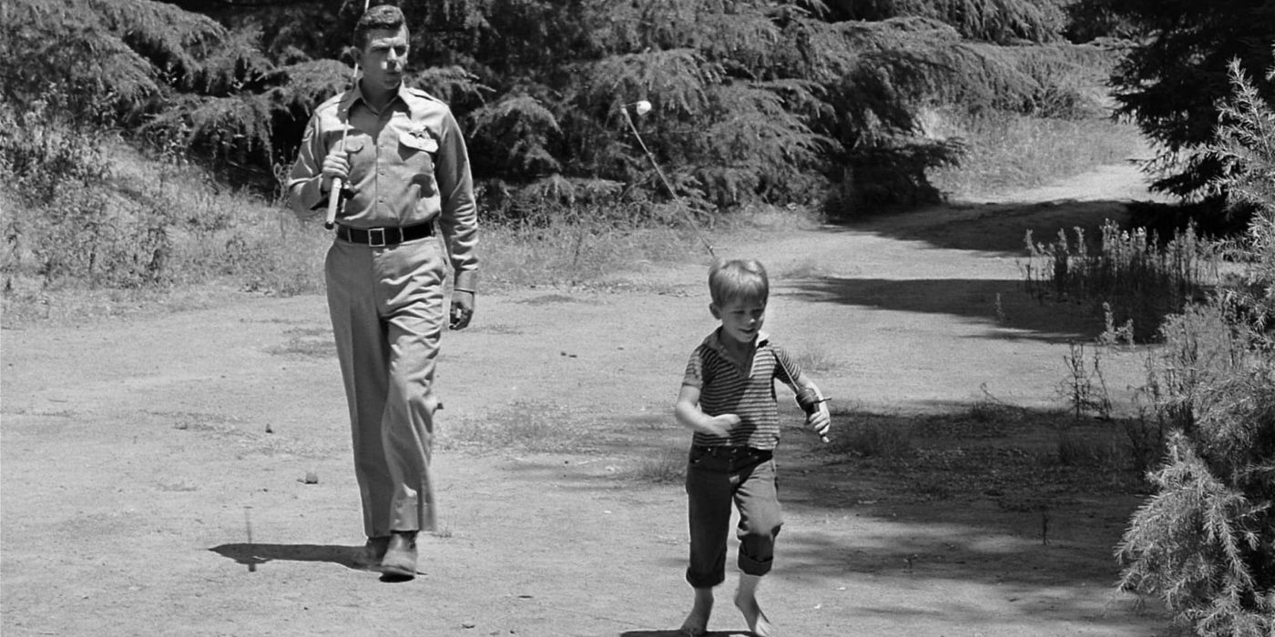 Andy Griffith and Ron Howard walking with fishing poles on a dirt path in 'The Andy Griffith Show.'