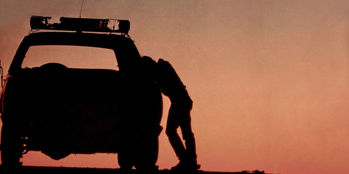 A silhouette of a person standing next to a police car with busted lights in 'The Hitcher'