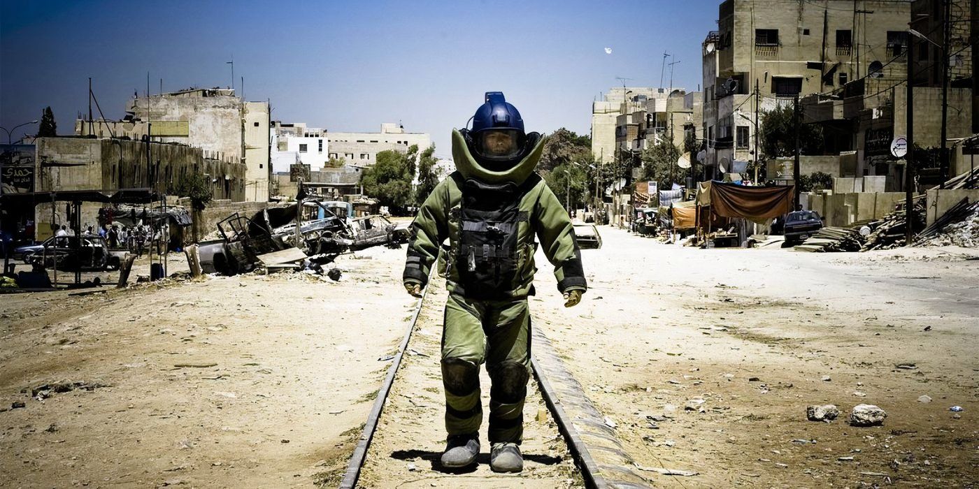 William James (Jeremy Renner) walks down a dusty street towards the camera wearing a bomb suit