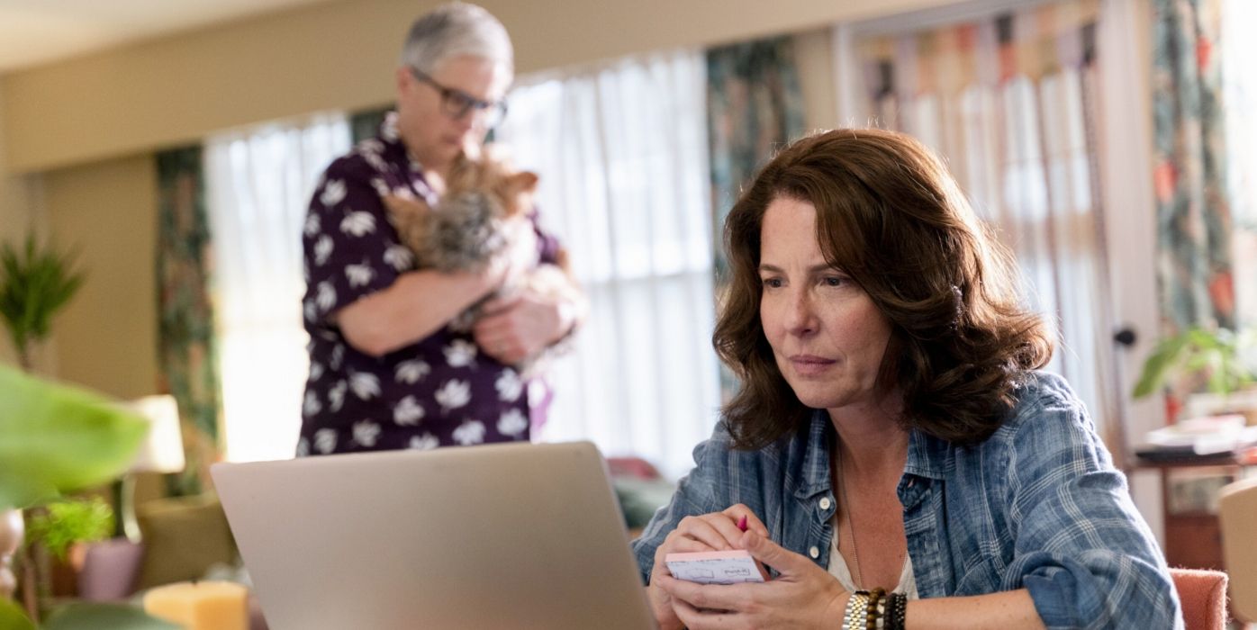 Teddi looks at a computer screen, while Velma stands holding a dog in the background in a scene from 'Tracker.'