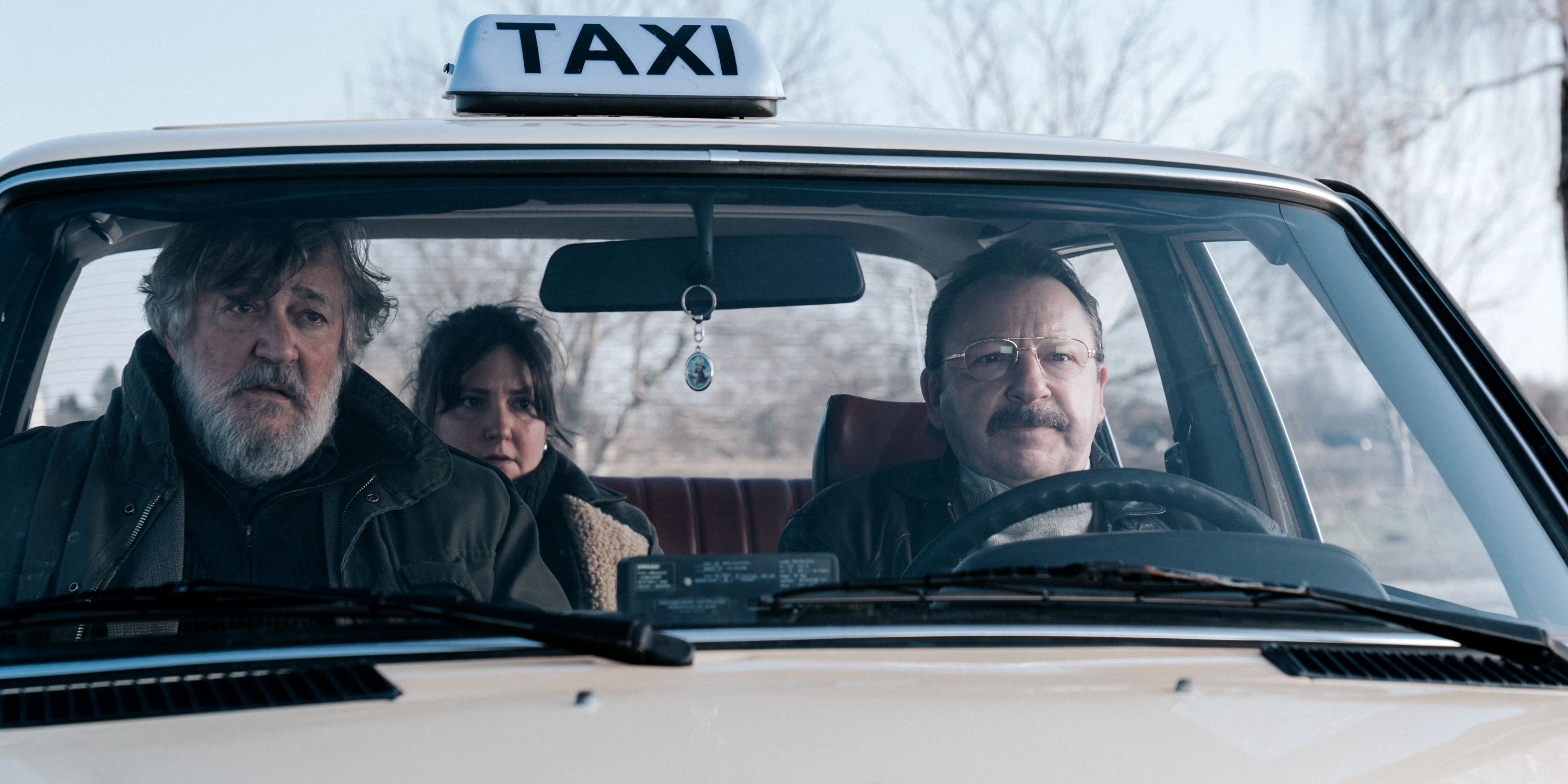 Lena Dunham como Ruth en el asiento trasero de un taxi y Stephen Fry como Edek en el asiento delantero en la película 