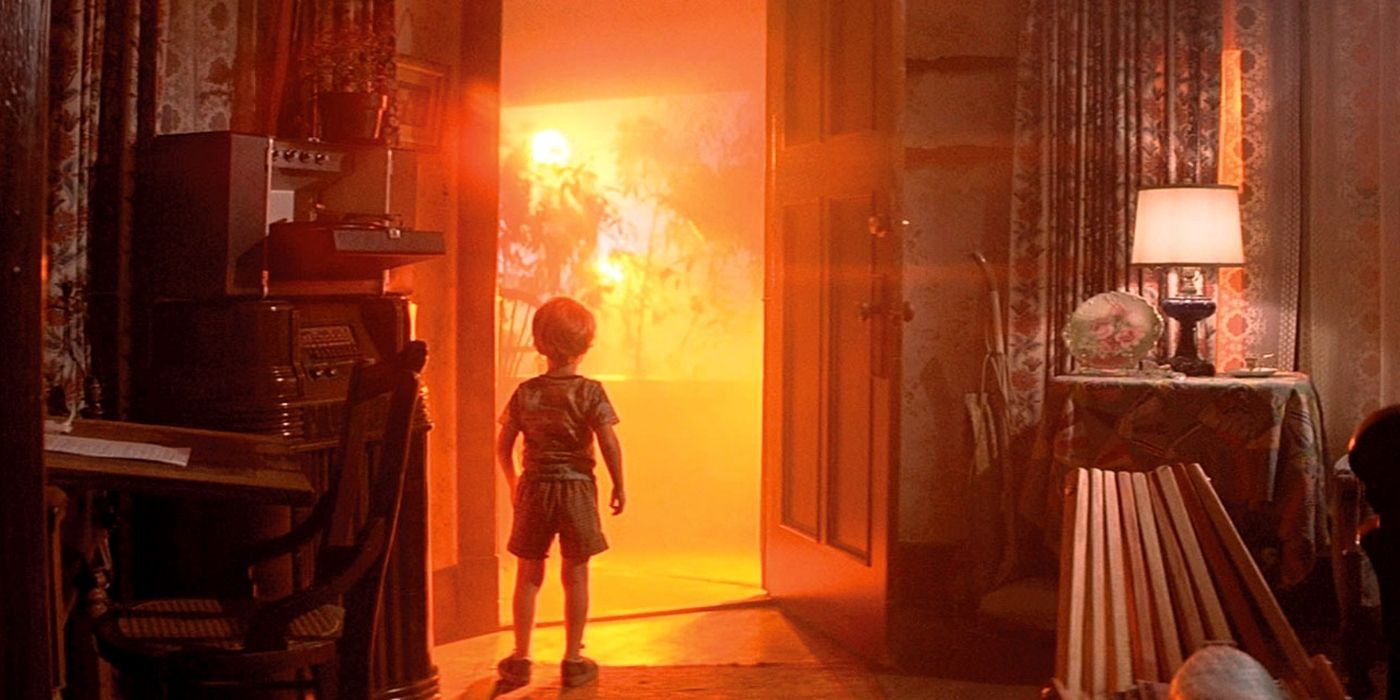 A child stares out an open front door where an ominous orange glow is coming though