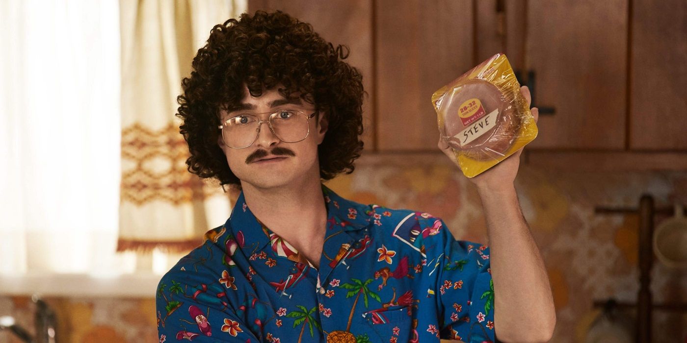 Daniel Radcliffe as Weird Al holding a snack in his kitchen in Weird: The Al Yankovic Story