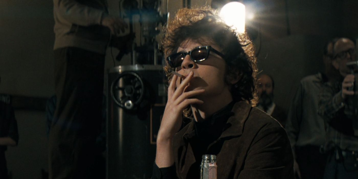 Timothee Chalamet as Bob Dylan in a studio wearing sunglasses and smoking a cigarette in A Complete Unknown.