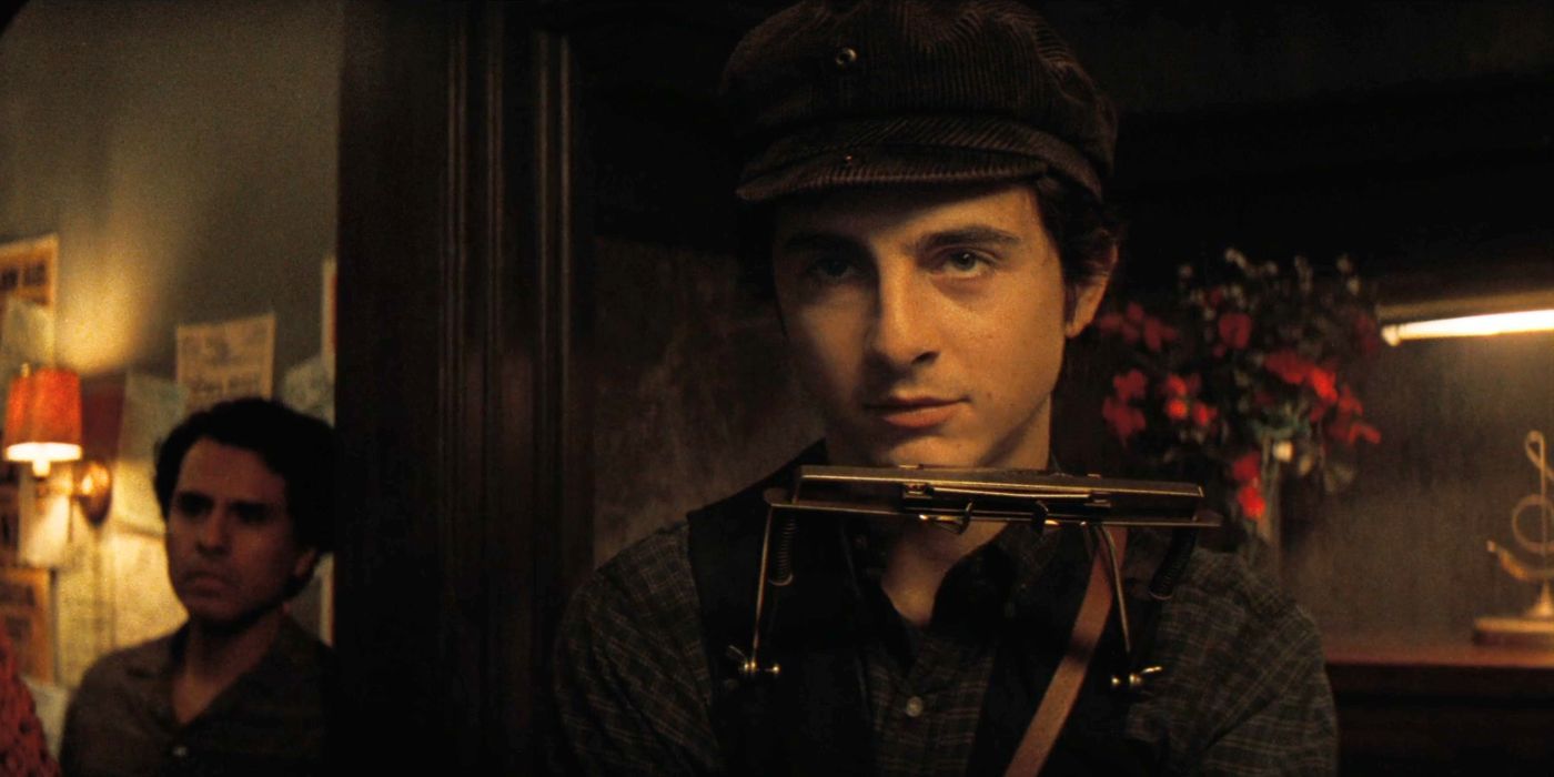 Timothee Chalamet as Bob Dylan with a harmonica close to his face in A Complete Unknown.