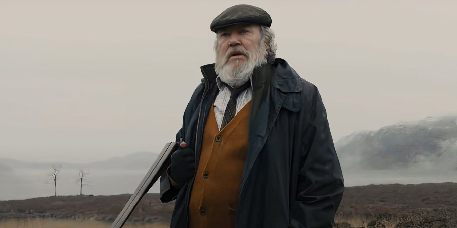 Albert Finney as James Bond's Gamekeeper Kincaid holding a rifle in a field in Skyfall