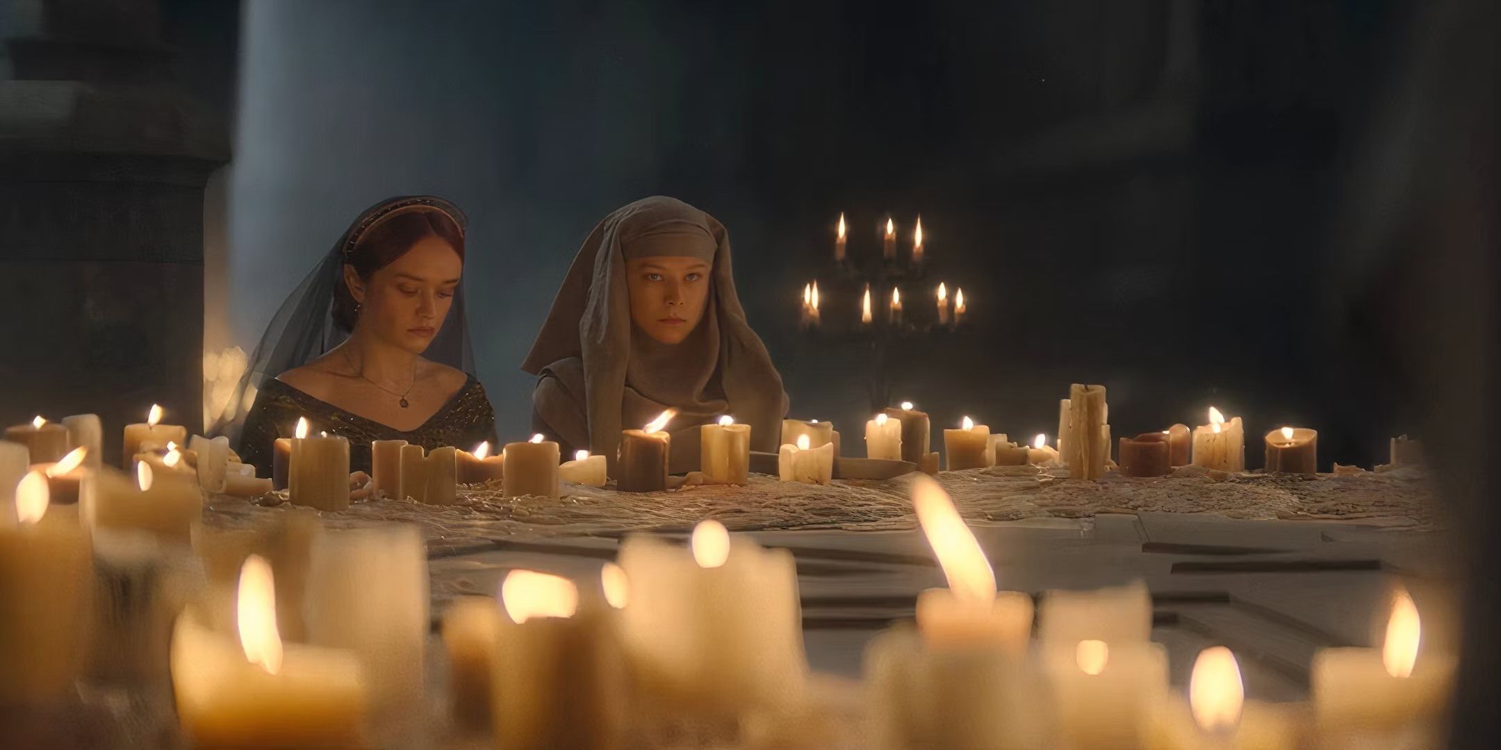 Olivia Cooke as Alicent Hightower and Emma D’Arcy as Rhaenyra Targaryen sitting next to eachother in front of a large circle of candles in House of the Dragon