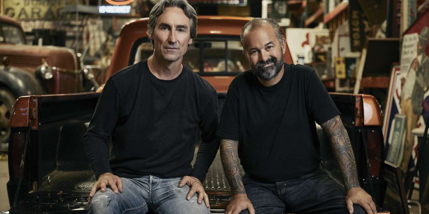 American Pickers Frank Fritz and Mike Wolfe sitting on a truck bed in a shop