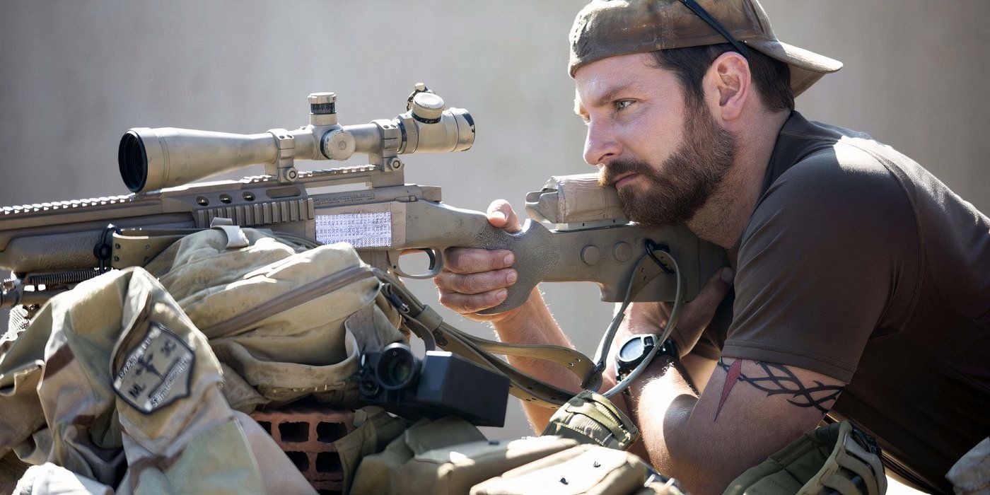 Bradley Cooper as Chris Kyle aiming a rifle over a wall of sandbags in American Sniper