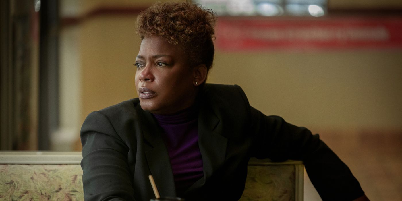 Aunjanue Ellis sitting at a table in a restaurant wearing a black jacket and looking slightly to her right.