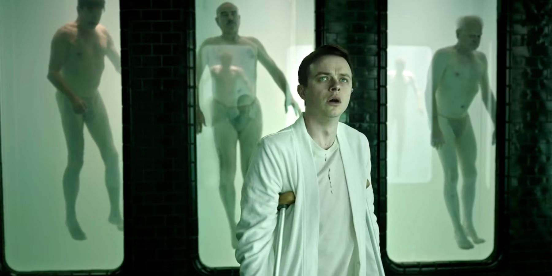 Dane DeHaan looking confused in a room with tanks with human bodies in A Cure for Wellness 