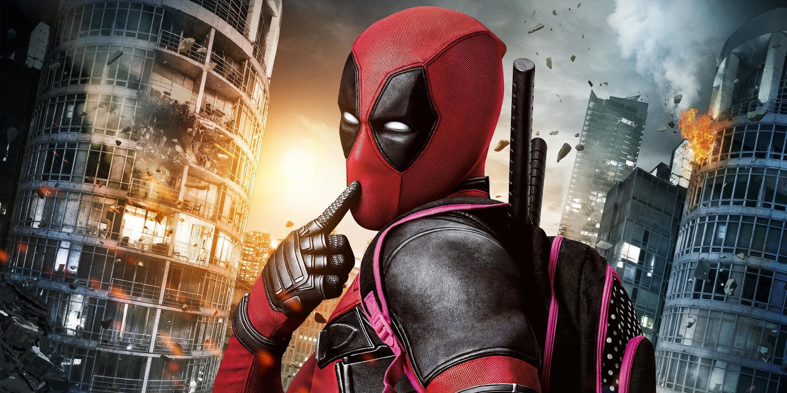 Deadpool with one finger on his mouth looking at the camera as buildings explode behind him