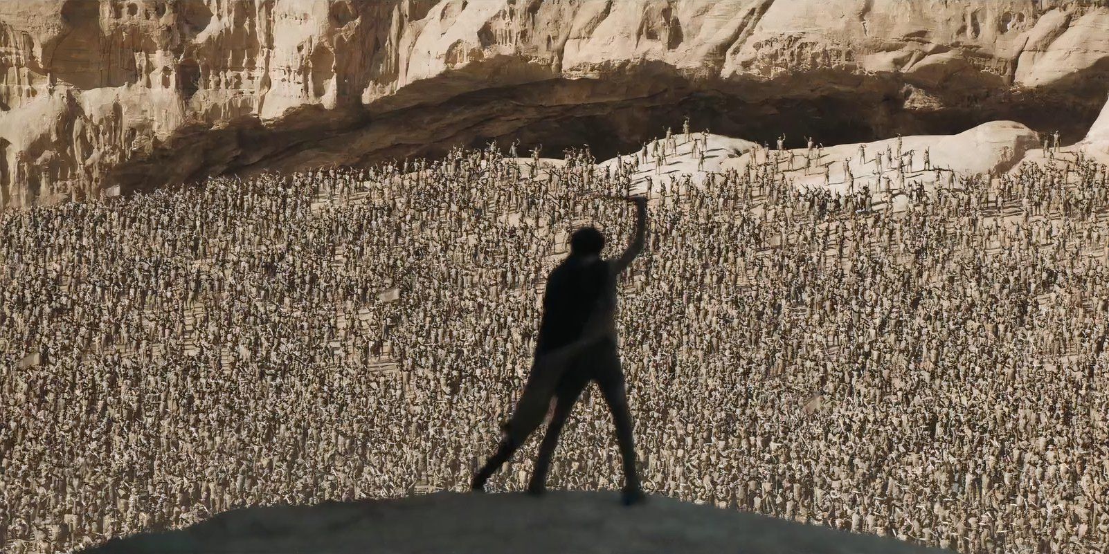 The silhouette of Paul Atreides (Timothee Chalamet) bearing a blade high above his head, stands before an awesome crowd.