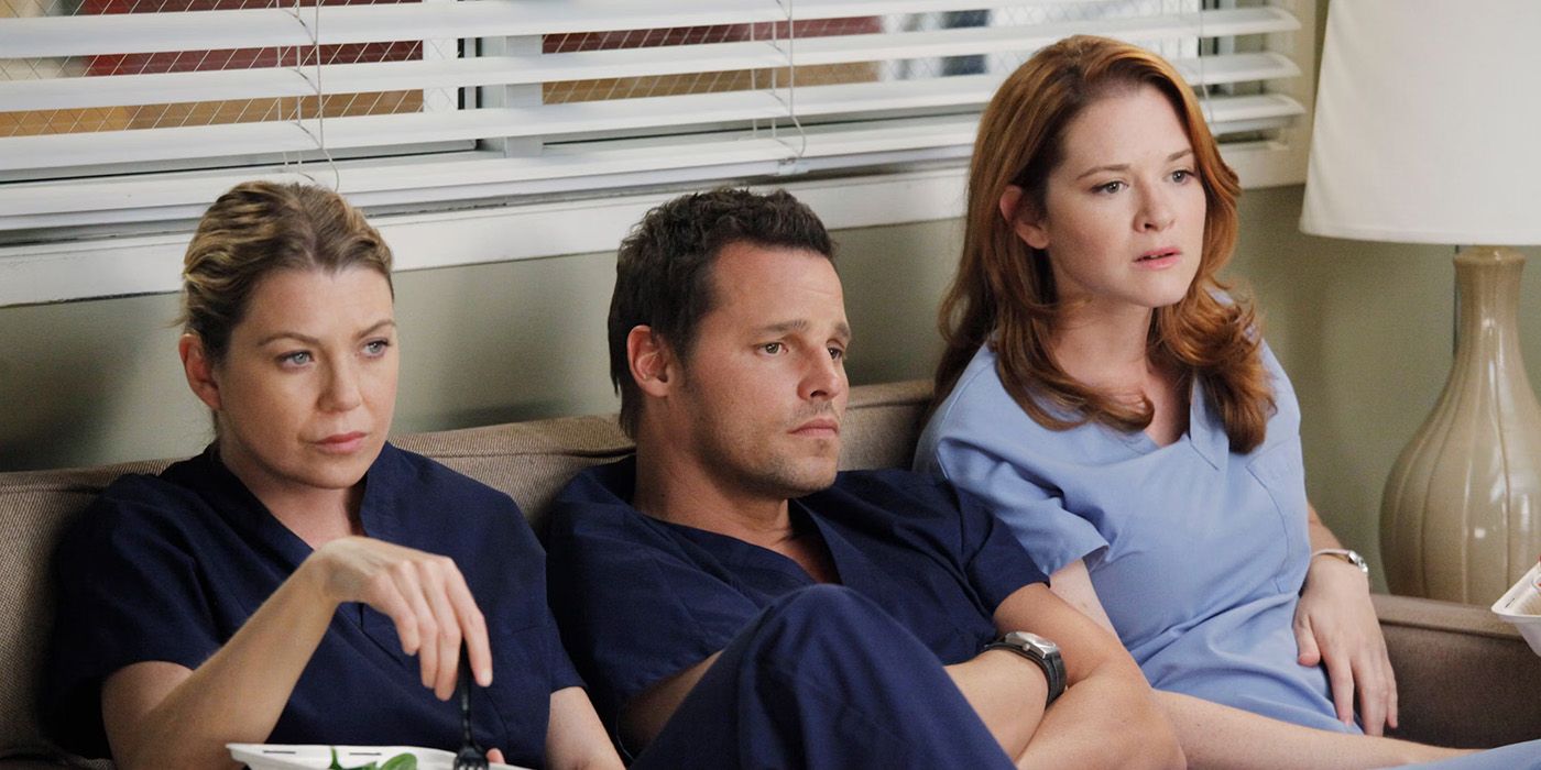 Ellen Pompeo, Justin Chambers, and Sarah Drew sitting on a couch wearing scrubs in Grey's Anatomy