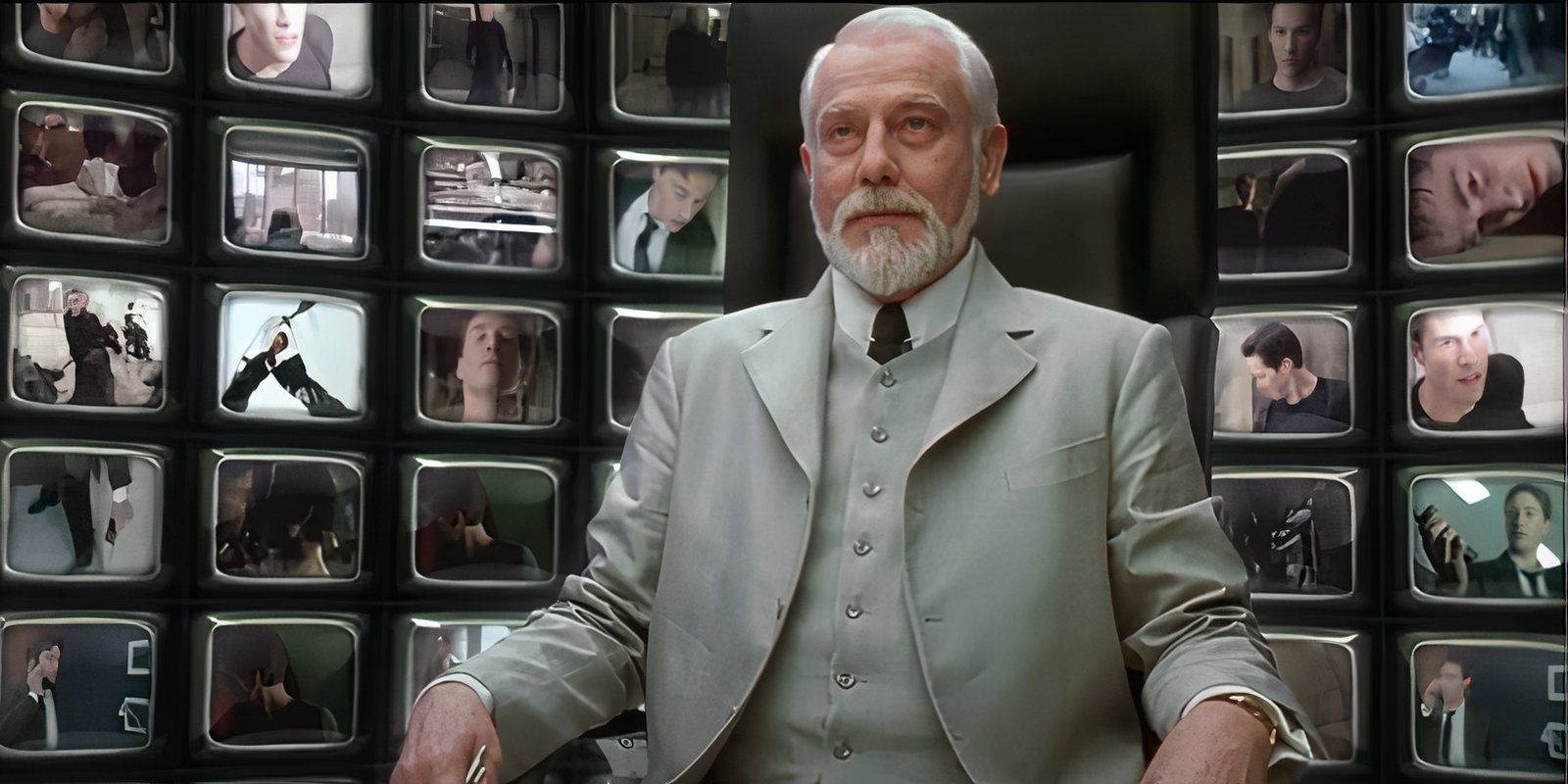 Helmut Bakaitis as the Architect sits in a chair surrounded by TV monitors in The Matrix Reloaded