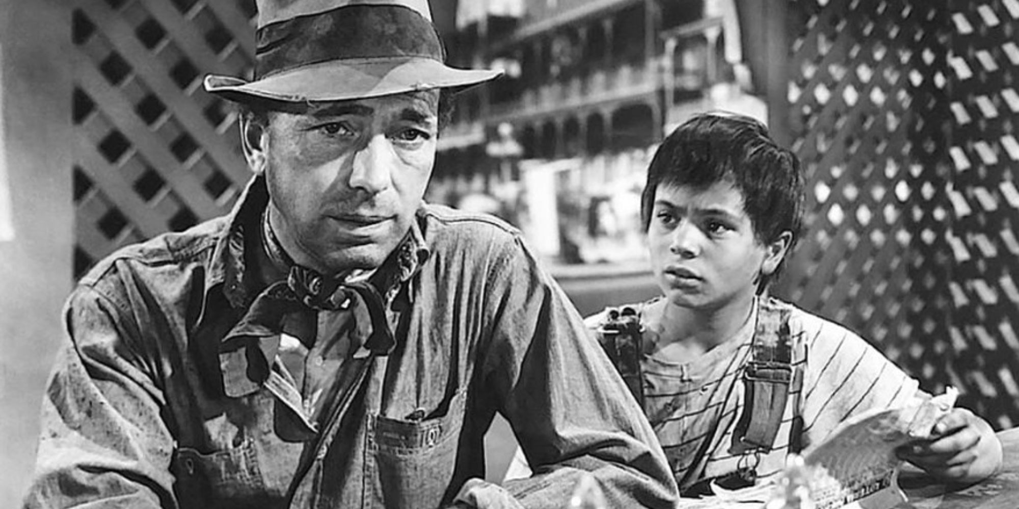 Humphrey Bogart sitting down while Robert Blake stands next to him looking at him in The Treasure of Sierra Madre (1948)