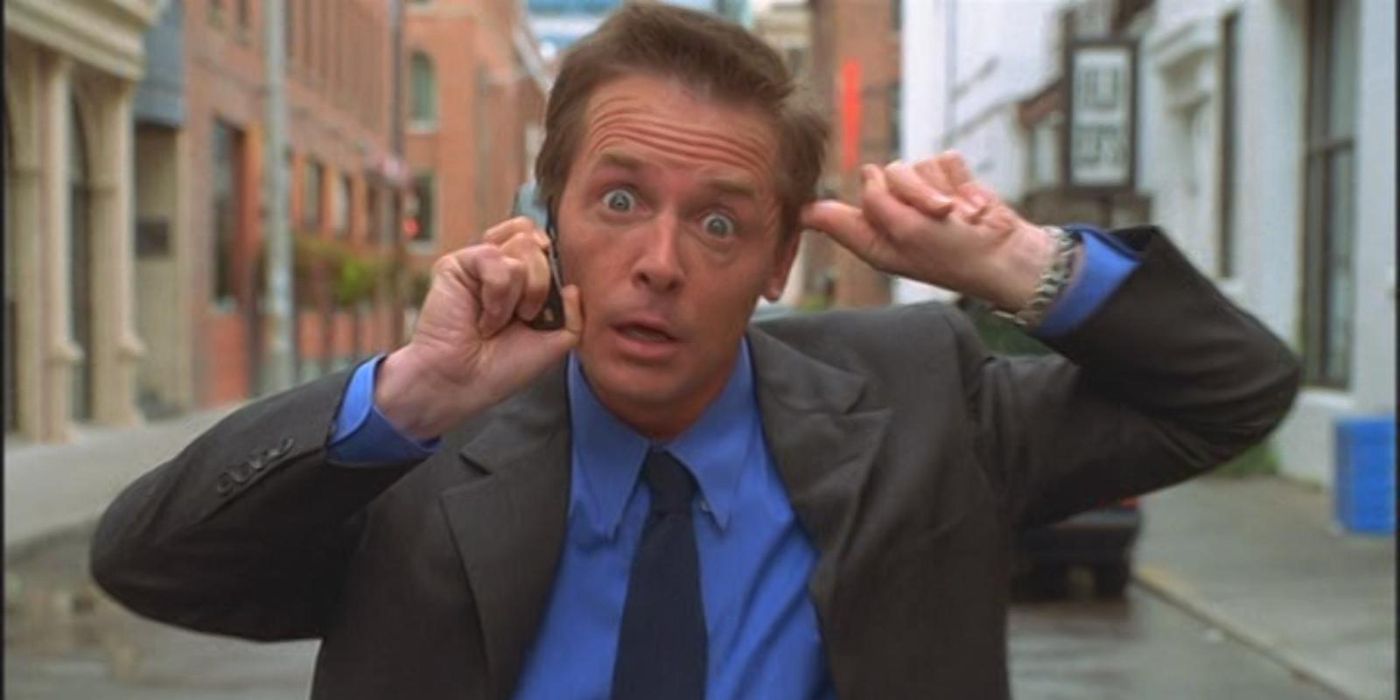 Mr. Baker (Michael J. Fox) stands in the middle of the road in a suit, blocking an ear as he talks on the phone in 'Interstate 60' (2002).