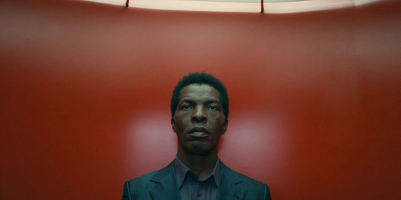 A man in a turquoise suit stands against a red wall in The Limits of Control