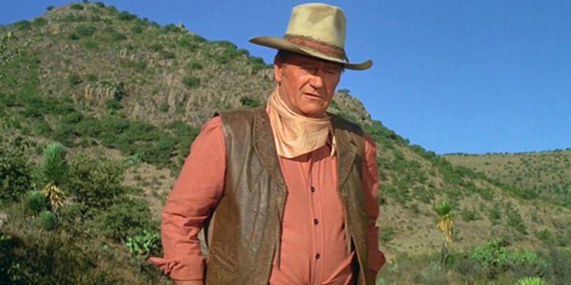 John Wayne wearing a cowboy hat and leather vest, standing on a mountainside in Big Jake (1971)