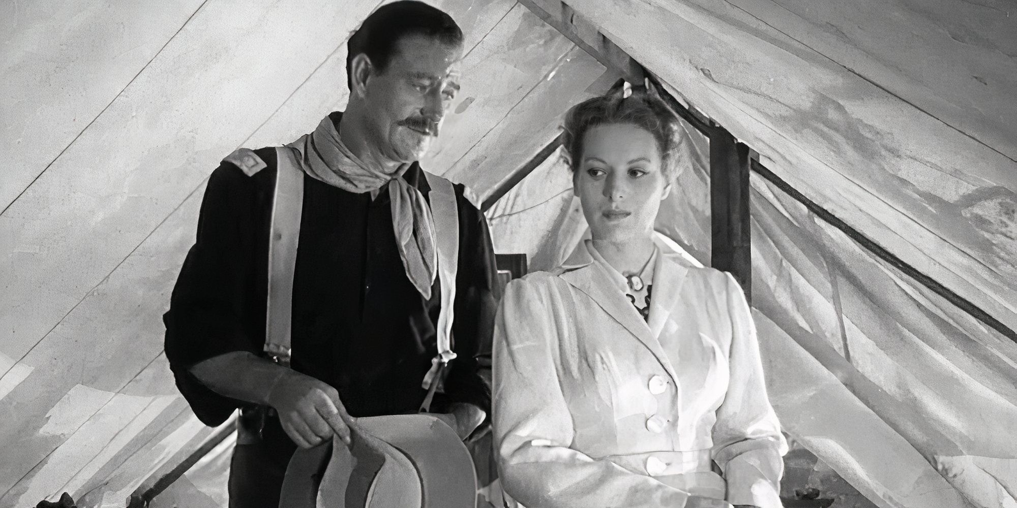 John Wayne standing close behind Maureen O'Hara in a tent in Rio Grande (1950)