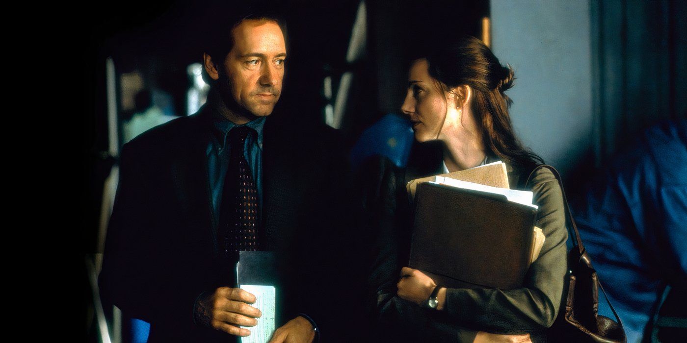 A man wearing a sport coat holds folders under his arm while looking at a smartly dressed woman holding a pile of folders in The Life of David Gale (2003)