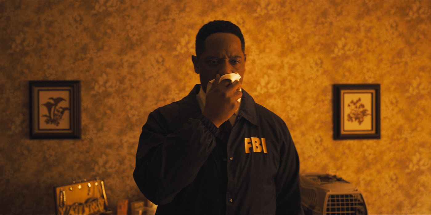 Blair Underwood holding up a handkerchief to his mouth with a look of horror in an orange-lit room